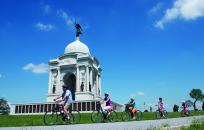 Family Riding Bikes next to a  Monument In Gettysburg